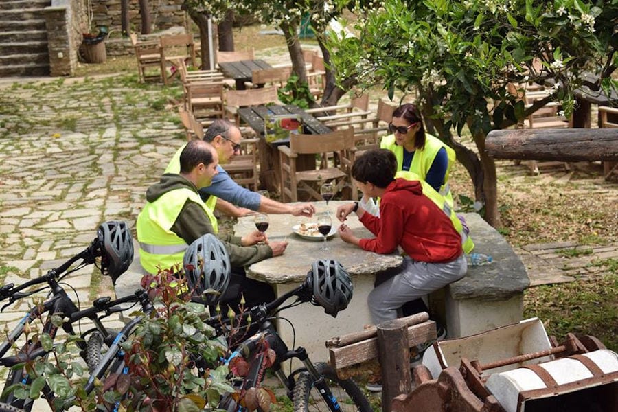 tourists with bikes sitting on a table outside Aristaios', drinking wine and eating delicacies